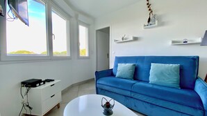 Een moderne woonkamer met een blauwe bank, een witte salontafel en een aan de muur bevestigde televisie.