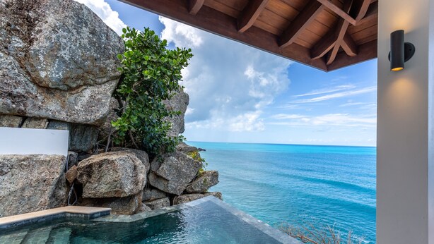 A clear view of a swimming pool with a view of the ocean, surrounded by large rocks and greenery. - M&M Cooper Bay - The Cooper Bay Villas (Road Town)