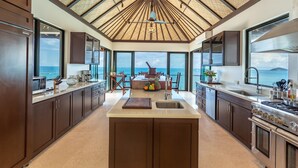 A modern kitchen with a large island, dark wooden cabinets, and a view of the ocean. - M&M Cooper Bay - The Cooper Bay Villas (Road Town)