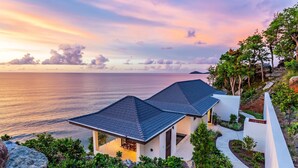 A modern house with a sloped roof, white walls, and a view of the sea at sunset. - M&M Cooper Bay - The Cooper Bay Villas (Road Town)