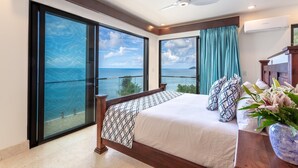 Un dormitorio con una cama grande, un ventilador de techo y vistas al océano a través de amplios ventanales.