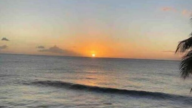 A sunset over the ocean with waves and a wooden fence in the foreground.