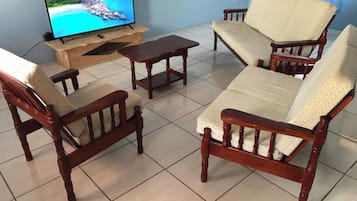 Una sala de estar con un sofá de madera, una mesa de centro y un televisor sobre un mueble de madera.