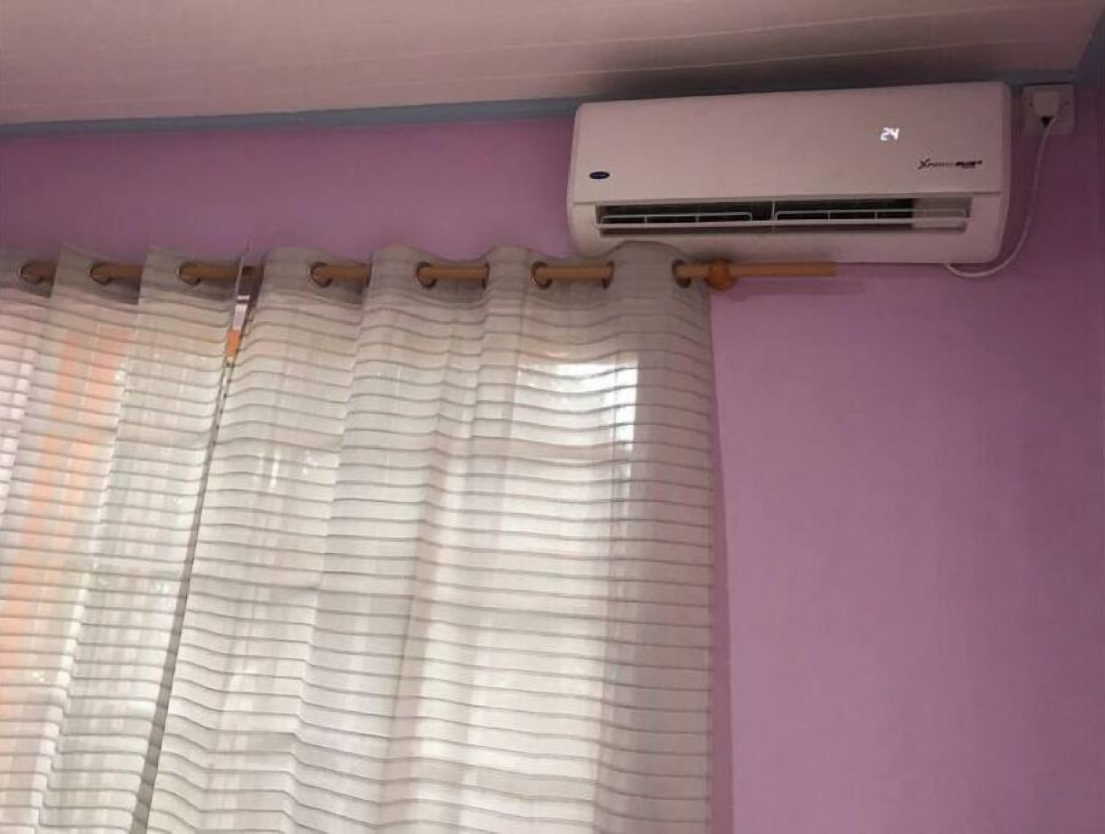 A room with a purple wall, a white air conditioning unit, and a striped curtain.
