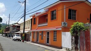 A street with buildings, including a brightly colored orange building with multiple windows and a white fence.