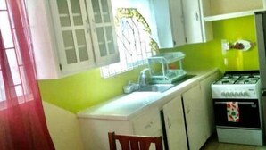 A compact kitchen with white cabinets, a gas stove, and a dining table with chairs. - Very clean 2-bedroom Apt. in St. Georges, Grenada (Saint George's)