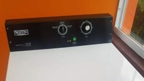 Eine weiße Maytag Waschmaschine mit Bedienfeld, in einem Raum mit orangefarbenen Wänden und einem Fenster.
