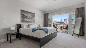 Ein modernes Schlafzimmer mit einem großen Bett, Blick auf die Stadt durch Schiebetüren und einem gerahmten Bild an der Wand.
