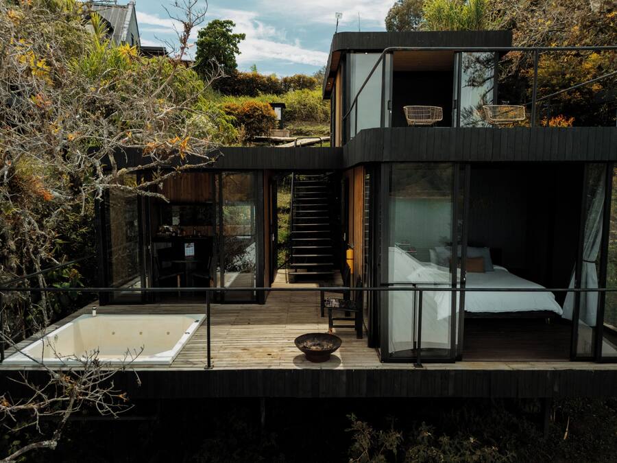 Una casa moderna con un dormitorio con paredes de cristal, una terraza de madera y un jacuzzi.