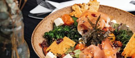Une table à manger avec une assiette de nourriture, un bocal en verre contenant des fleurs séchées et un verre à vin.