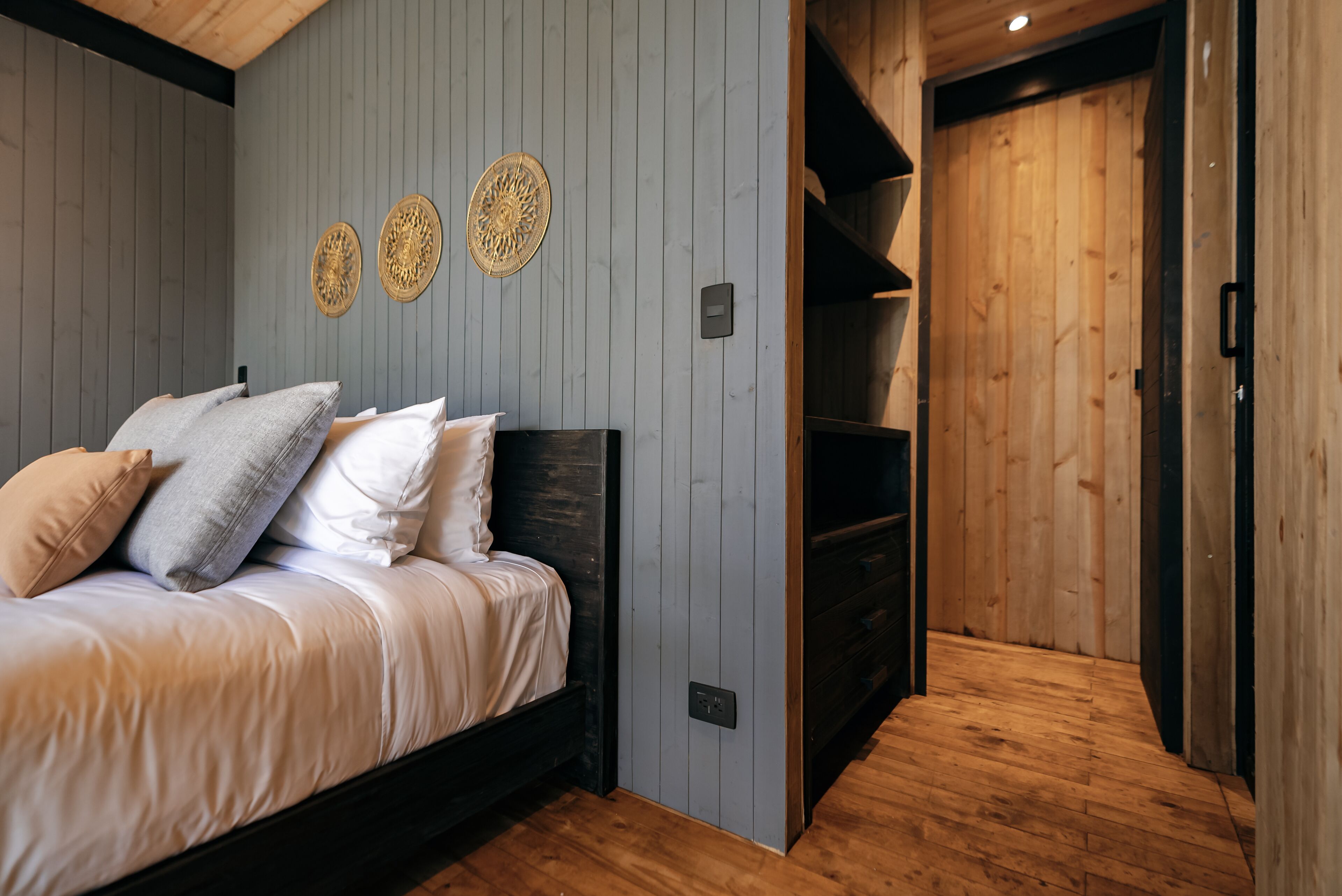 A bedroom with a bed, wooden floor, and a wooden door leading to another room.