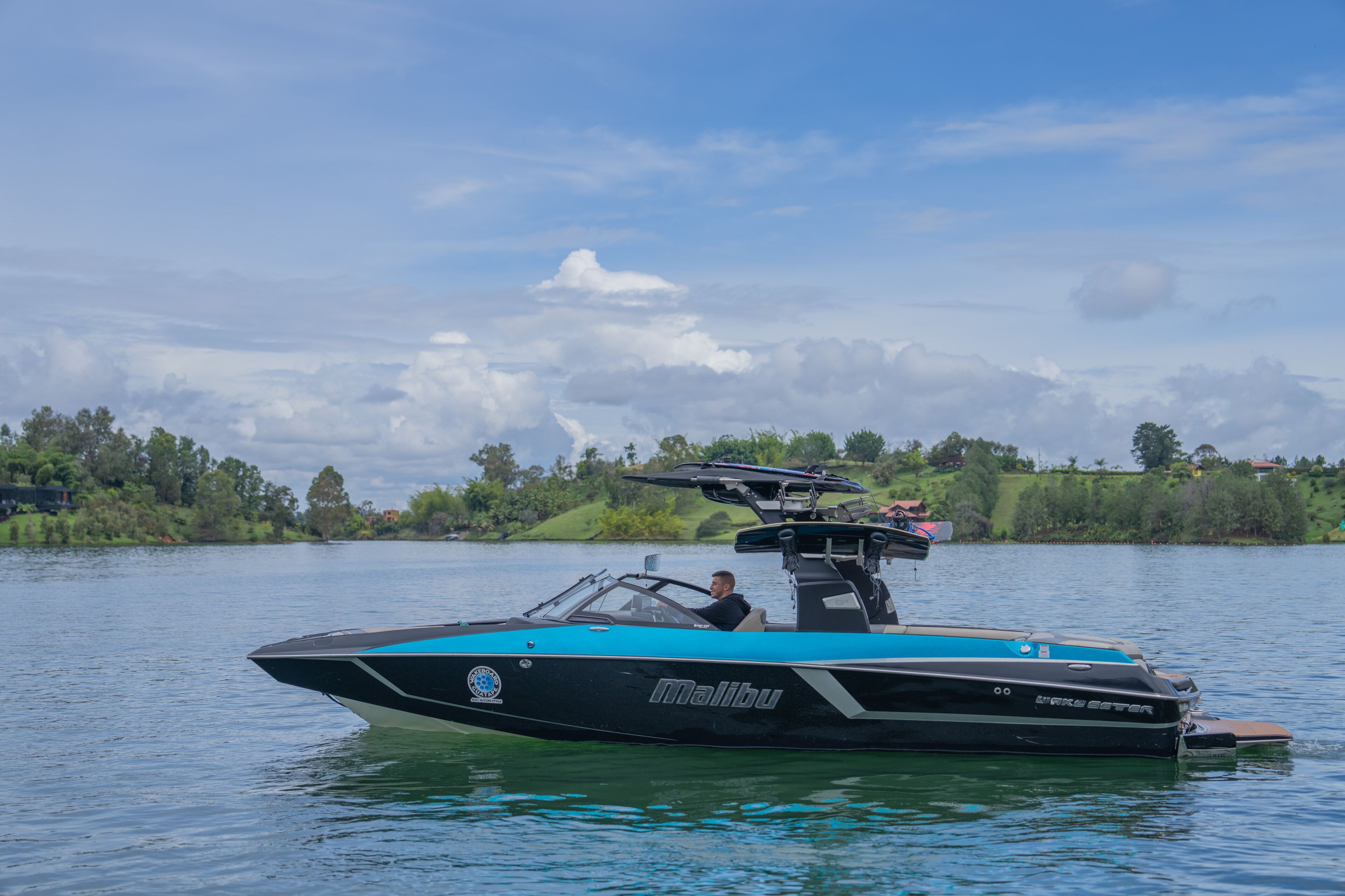 A Malibu speedboat on a calm lake with a clear sky.