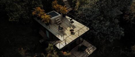 A wooden deck with outdoor seating, surrounded by dense foliage.