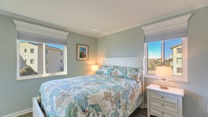 A bedroom with a bed, two windows, a nightstand, and a lamp. - Emerald Isle Vacation Rental w/ Resort Pool! (Emerald Isle)