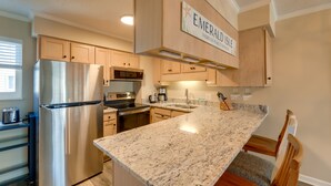 A modern kitchen with a stainless steel refrigerator, granite countertop, wooden cabinets, and a sign that reads "Emerald Isle." - Emerald Isle Vacation Rental w/ Resort Pool! (Emerald Isle)