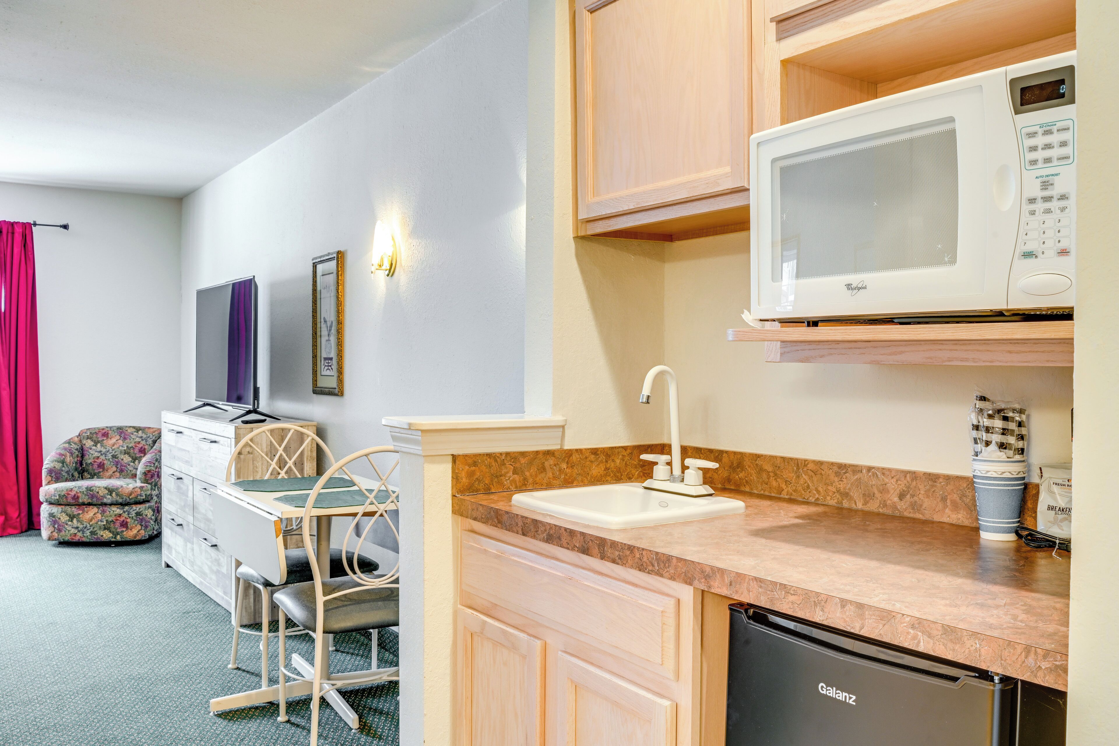 A compact kitchenette with a microwave, sink, and dishwasher. A small dining area with a chair and table is visible.