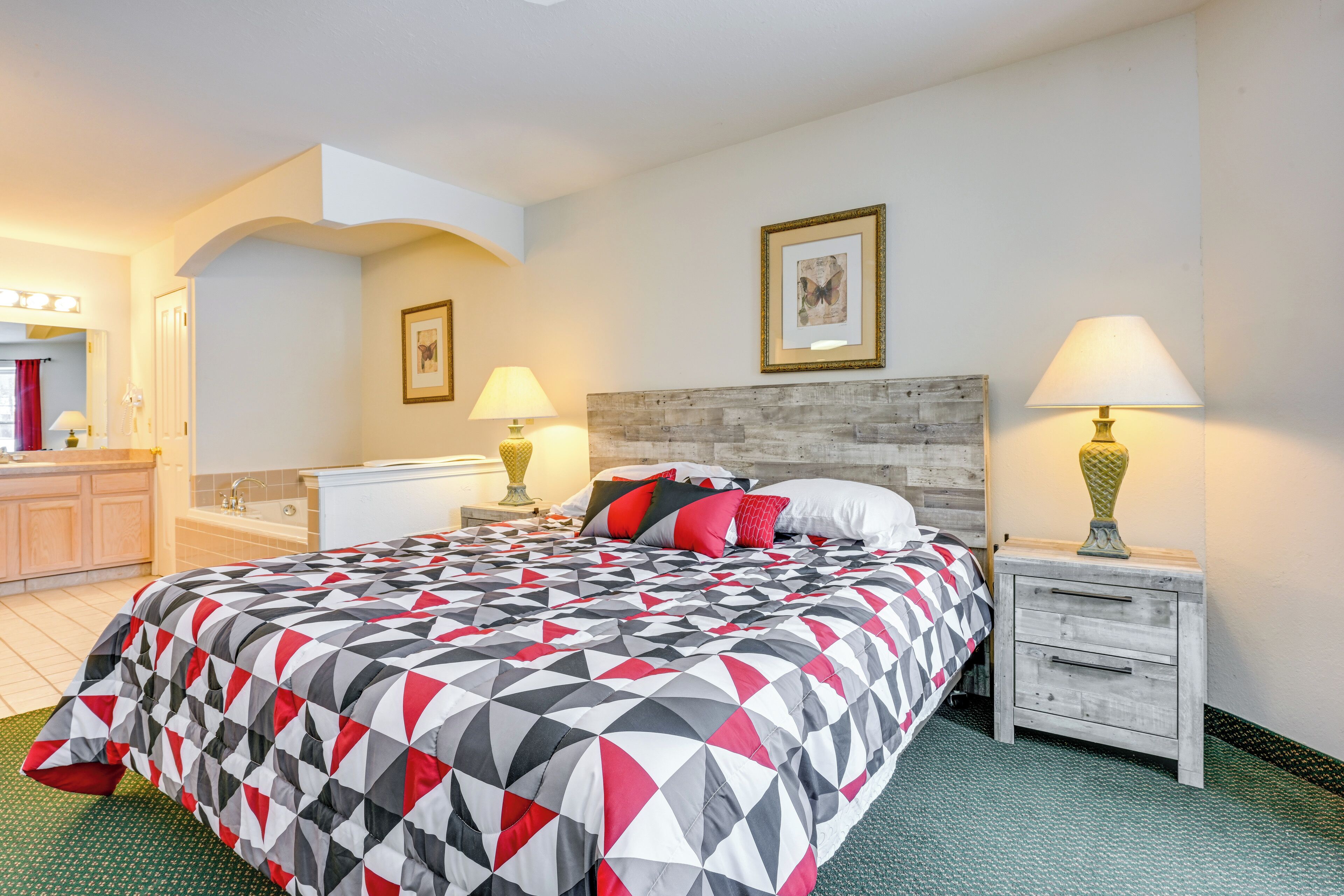 A hotel room with a bed, two bedside tables with lamps, a headboard, a bathroom with a sink and mirror, and a green rug.