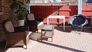 Un patio al aire libre con mobiliario de mimbre, una planta en maceta y una cerca roja al fondo.
