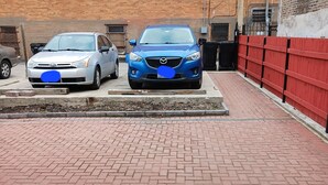 Un área de estacionamiento con dos autos, pavimento de ladrillo y una cerca roja.