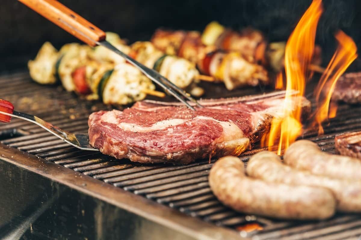 Una parrilla con un bistec, salchichas y brochetas de verduras a la cocción.