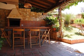 An outdoor patio with a stone wall, a brick oven, and wooden chairs. - Villa 350 meters from the sea - CIR: 19088009C223120 CIN: IT088009C2ZLVAKRMU  (Marina di Ragusa)
