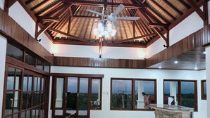 A spacious room with large windows, a ceiling fan, and a stone accent wall. - NEW Stunning 3 bed Luxury Balinese Villa with Panoramic Ocean Views and Pool (Bali)