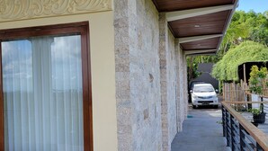 A covered outdoor area with stone walls, a wooden bench, and a white car parked in the background. - NEW Stunning 3 bed Luxury Balinese Villa with Panoramic Ocean Views and Pool (Bali)