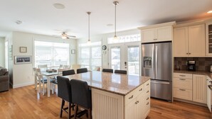 Una cocina moderna con una isla central, electrodomésticos de acero inoxidable y un comedor con ventilador de techo.