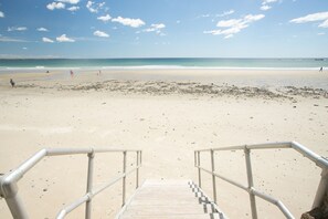 Una playa con una escalera metálica que lleva a la orilla, arena y el océano.