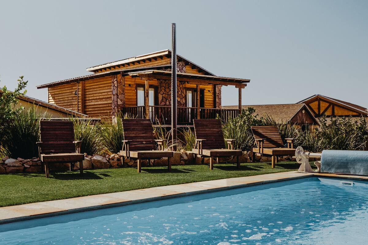 A pool area with a wooden house, lounge chairs, and a stone pathway.