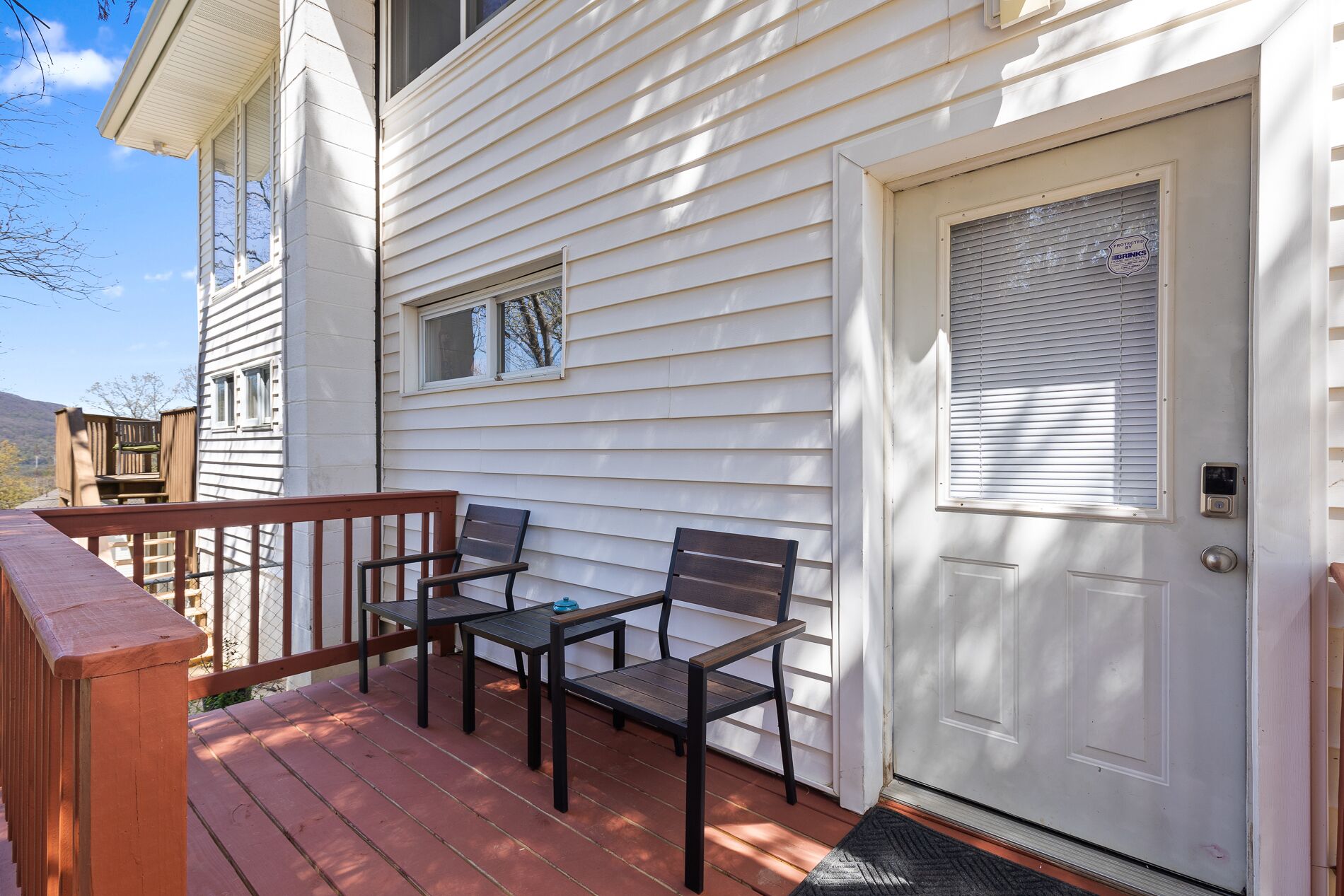 A porch with two chairs and a table, a white door with a window, and a small window above the door.