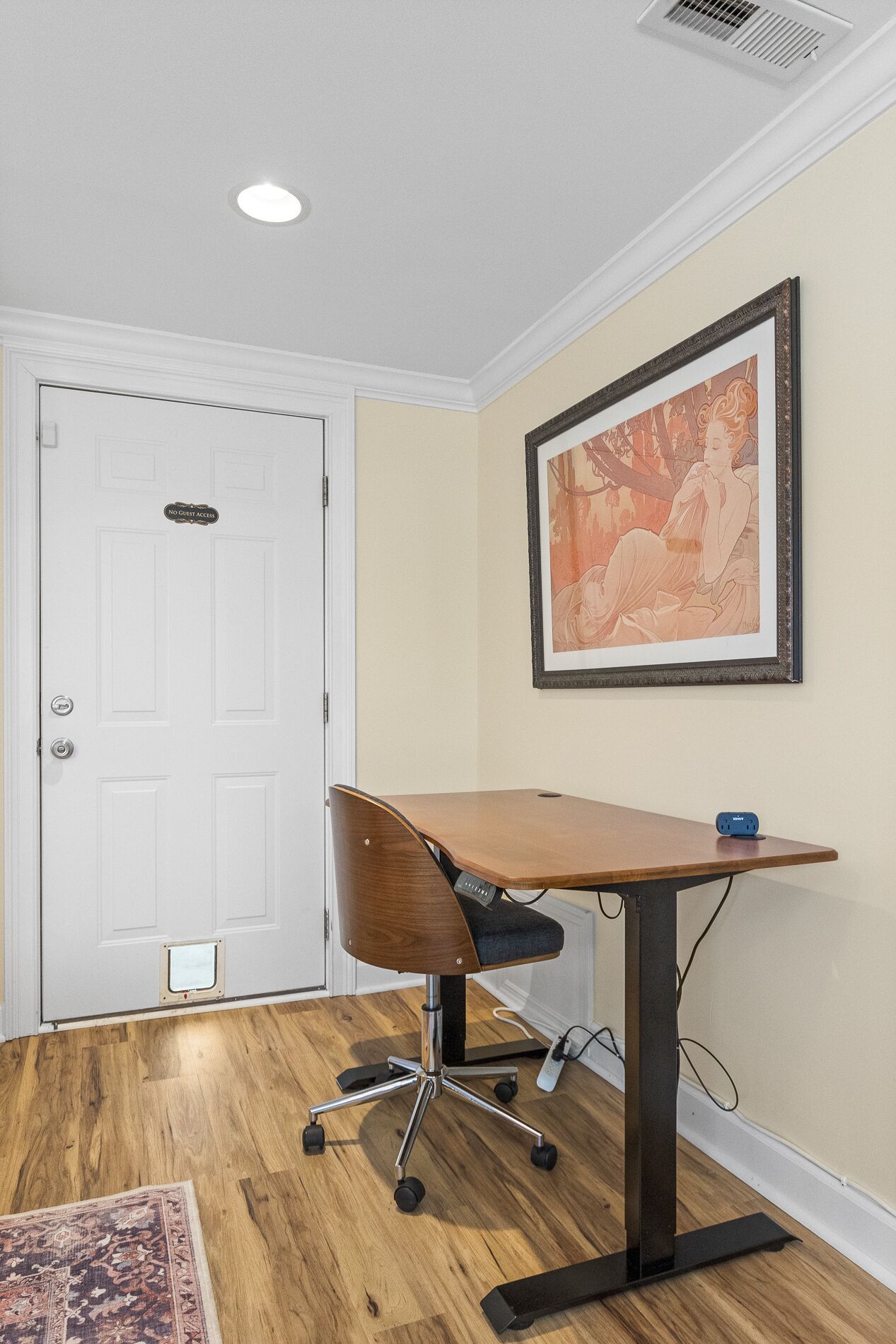 Une salle de conférence avec une table en bois, un fauteuil de bureau moderne, une œuvre d’art encadrée au mur et une porte blanche portant une pancarte indiquant « Accès interdit aux visiteurs ».