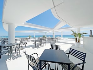 An outdoor seating area with tables and chairs, a potted plant, and a view of the ocean.