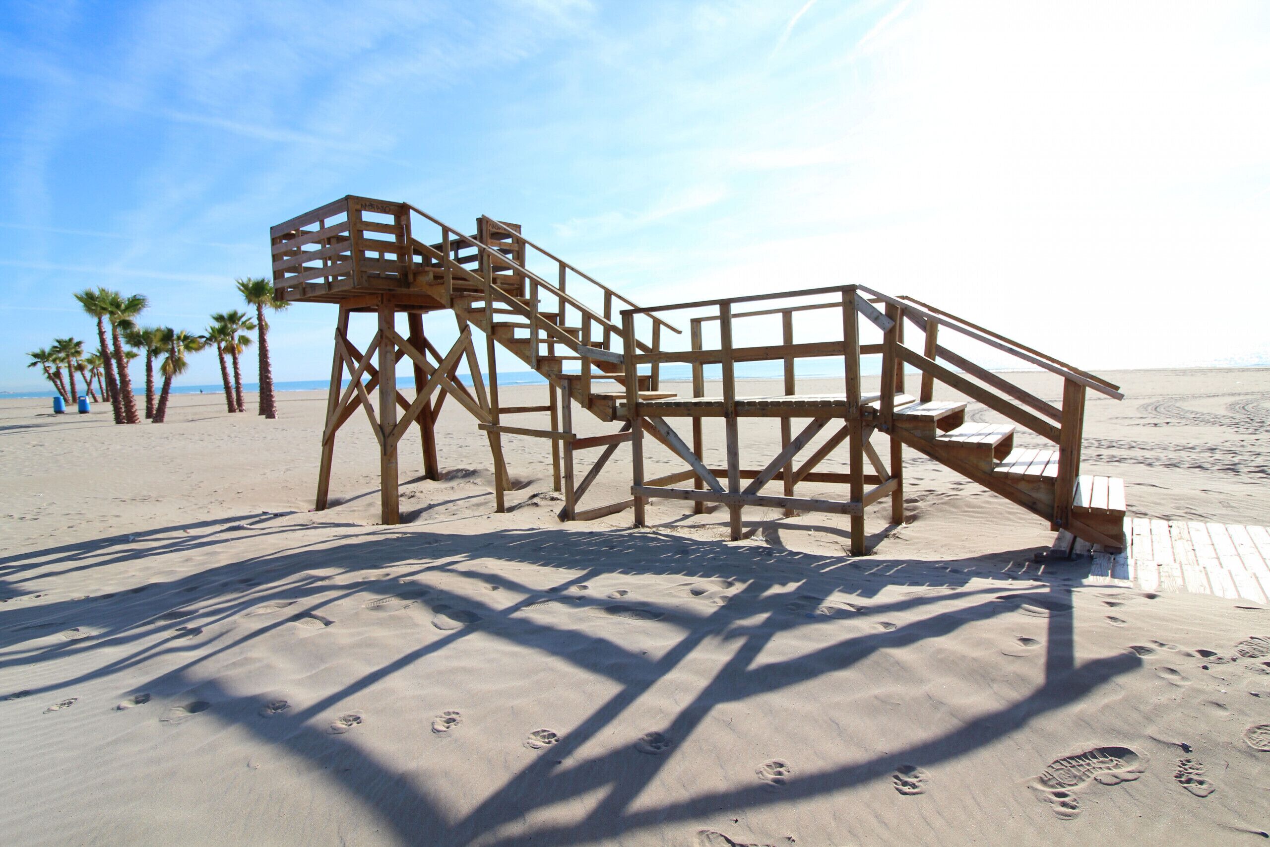 Une tour de surveillance en bois, sur une plage de sable, avec des palmiers en arrière-plan.