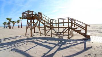 Une tour de surveillance en bois, sur une plage de sable, avec des palmiers en arrière-plan.