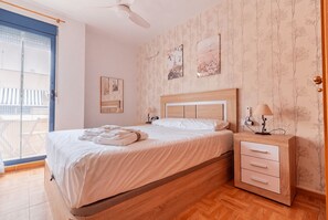 A neatly made bed with white linens and towels, a bedside table with a lamp, and a wall with framed pictures.
