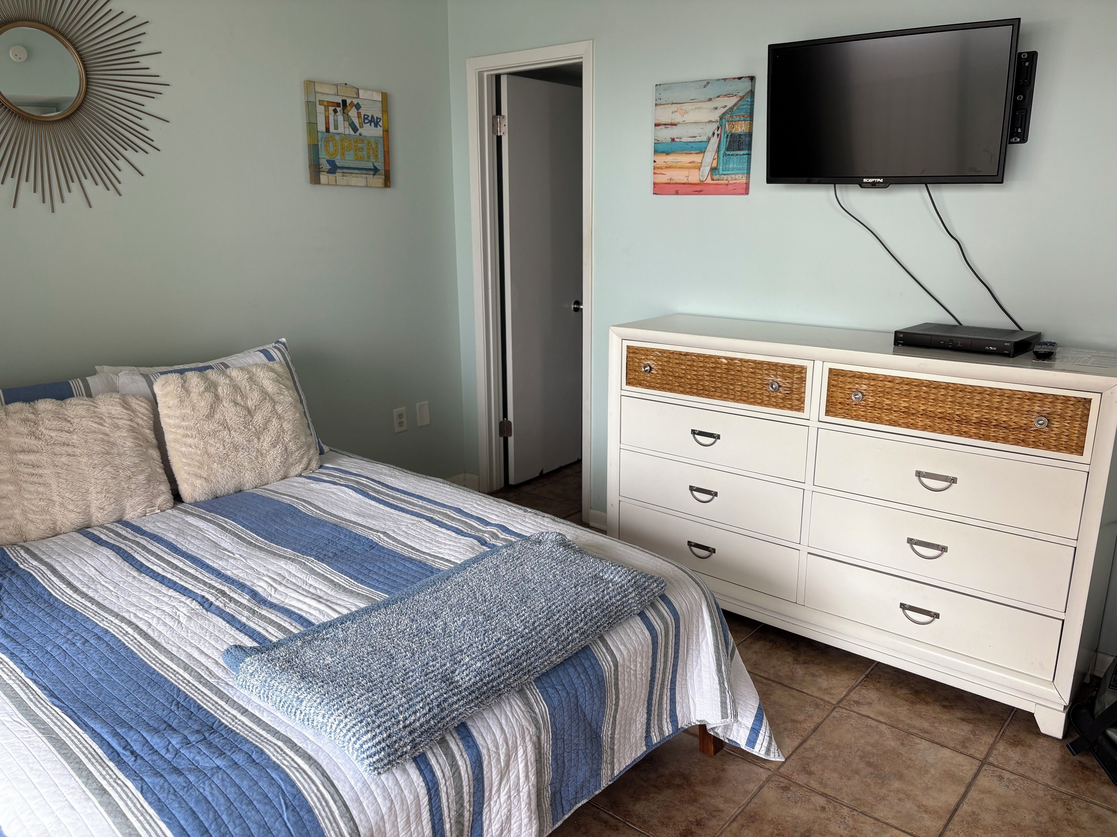 A bedroom with a bed, a dresser, a television, and a door.
