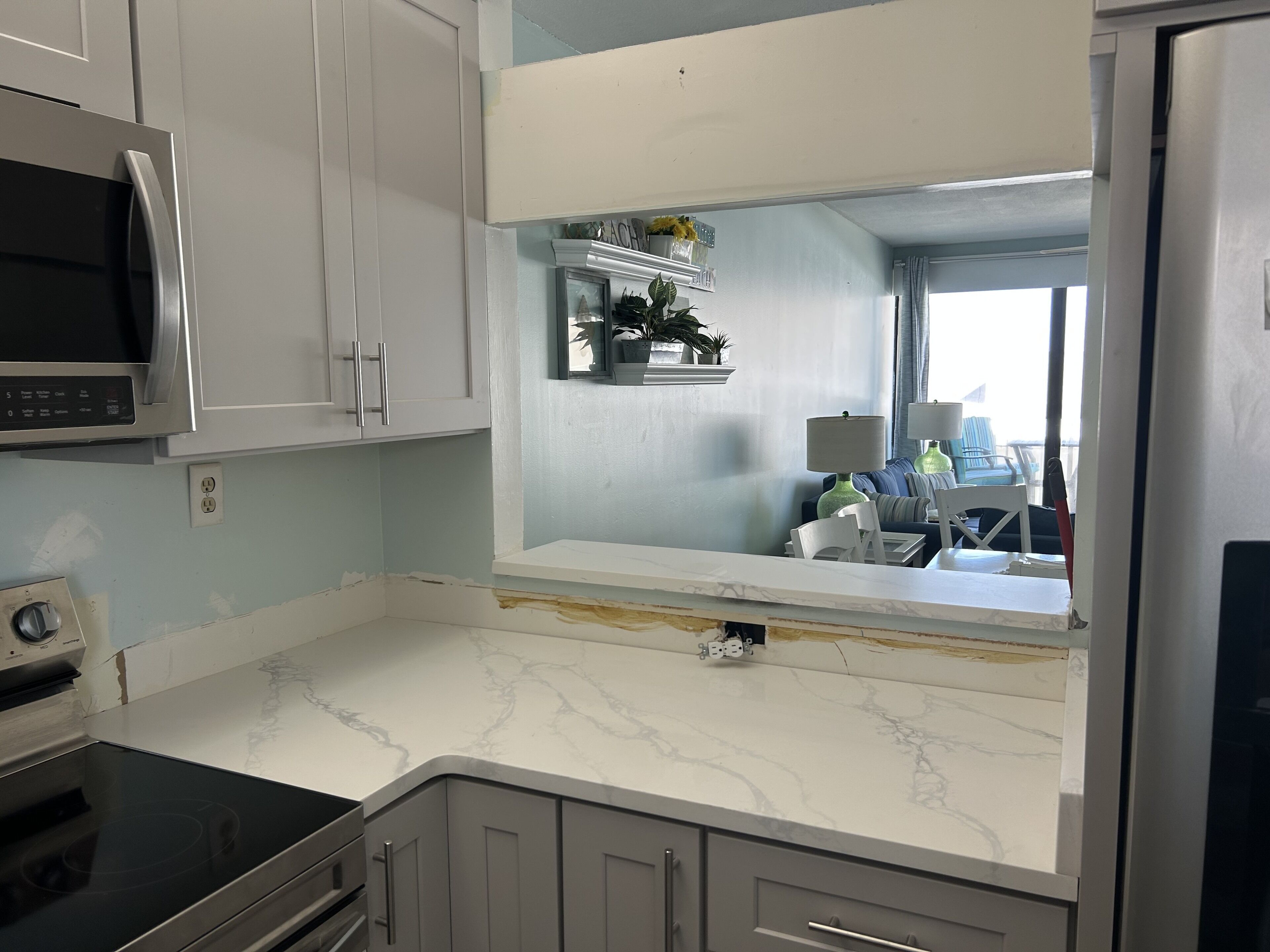 A kitchen with white cabinets, a built-in microwave, a marble countertop, and a view of a balcony with outdoor furniture.