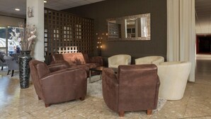 Un vestíbulo con sofás de cuero marrón, un sillón blanco, una mesa de centro de madera y un espejo decorativo en la pared.