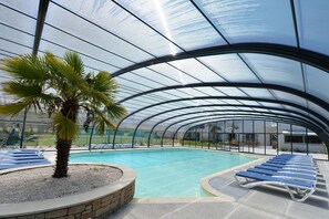 A covered swimming pool with lounge chairs and a palm tree. - Inter Hotel Carnac Nord du Golf de Saint Laurent (Ploemel)