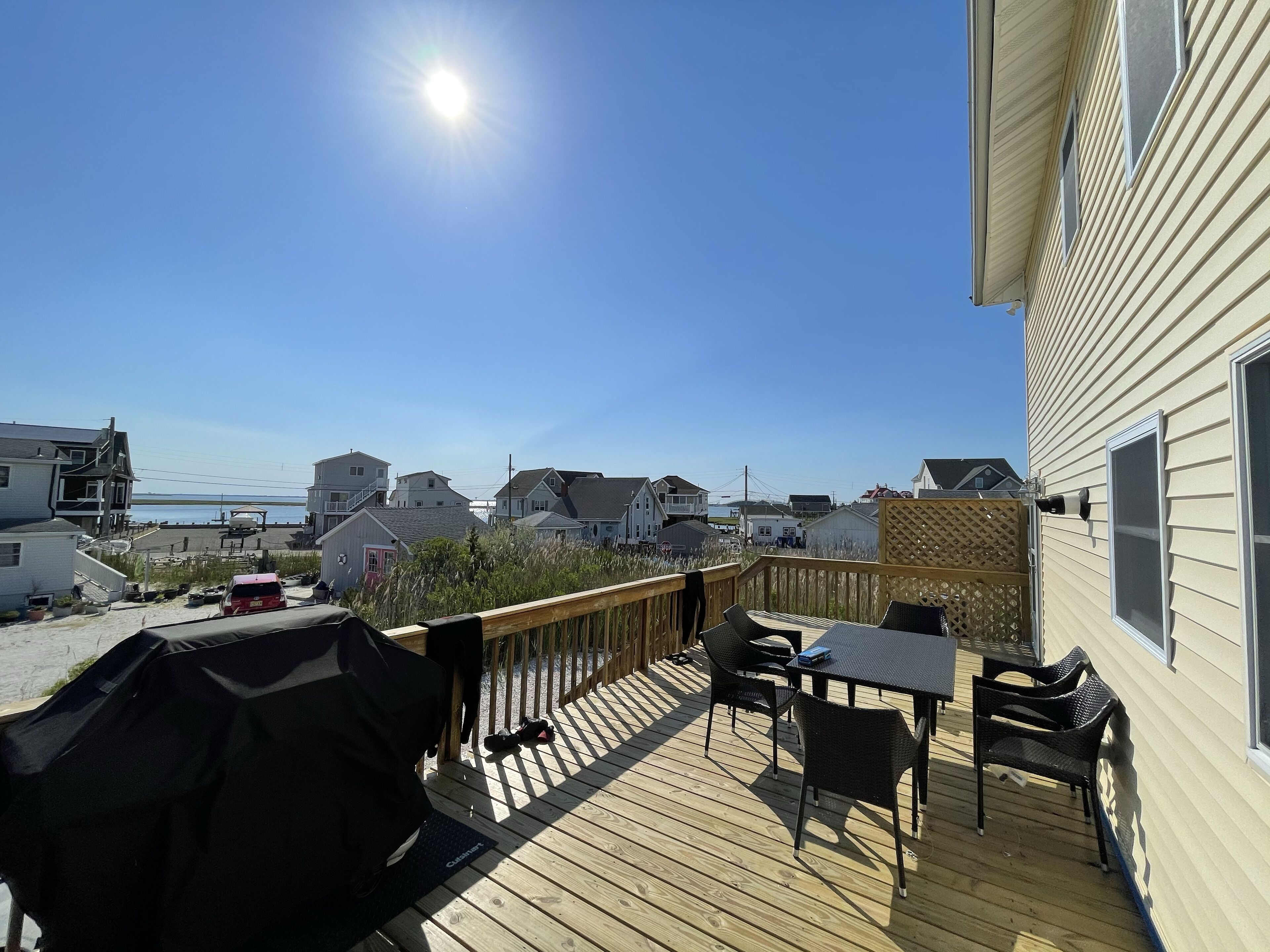 Une terrasse dotée de mobilier d’extérieur et d’un barbecue, offrant une vue sur un quartier résidentiel avec des maisons et une plage.