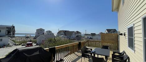 Une terrasse dotée de mobilier d’extérieur et d’un barbecue, offrant une vue sur un quartier résidentiel avec des maisons et une plage.