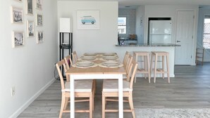 Un coin repas avec une table en bois dressée pour six personnes, entourée de chaises, dans une cuisine moderne où l’on aperçoit un réfrigérateur et un évier à l’arrière-plan.
