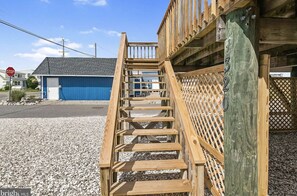 Un escalier en bois mène à un bâtiment dont la porte est bleue, et on aperçoit un panneau de signalisation en arrière-plan.