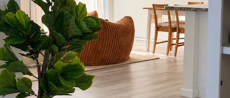Una sala de estar moderna con piso de madera, una planta grande en maceta, un sofá y un televisor de pantalla plana montado en la pared.