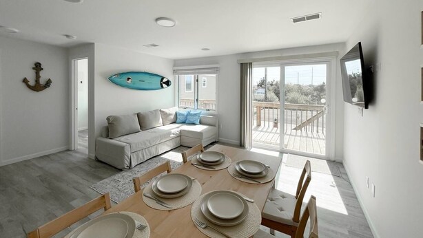 Un salon moderne comprenant un coin repas, un canapé, une planche de surf accrochée au mur et un balcon avec une balustrade.