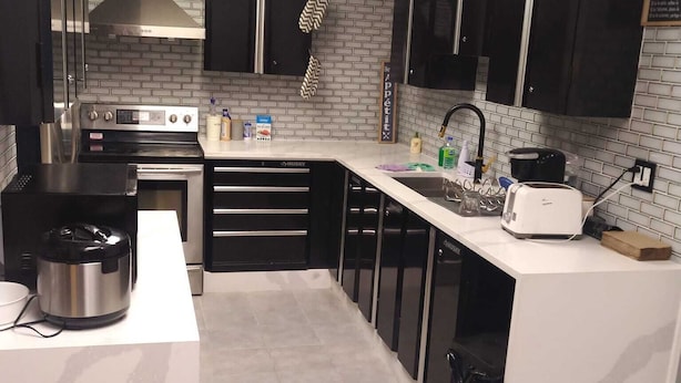 A modern kitchen with black cabinets, stainless steel appliances, and a white countertop.