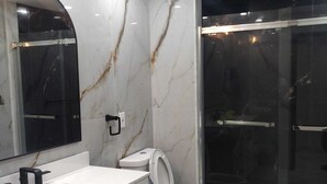 A modern bathroom with a white marble vanity, a toilet, and a glass-enclosed shower.