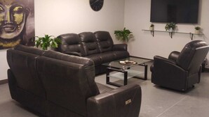 A modern living room with a sofa, two armchairs, a coffee table, a flat-screen TV, a clock, and two potted plants.