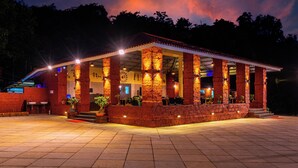 A covered outdoor area with a tiled floor, a building with a tiled roof, and columns. - Chinar Wood Resort Dapoli (Dapoli)